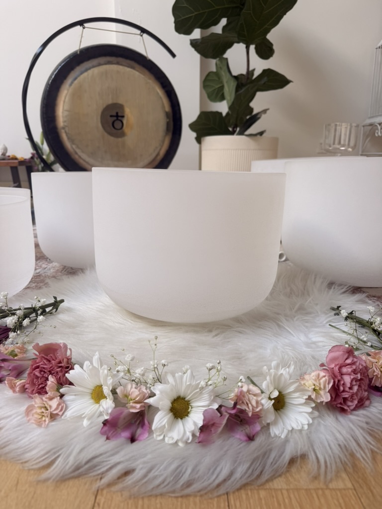 Crystal singing bowls framed by fresh flowers at Sanctuary+Health